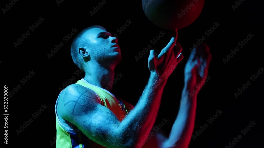 Young man, basketball player spinning basketball ball on his finger at studio over dark background in neon. Sport, action, motion, skill concept Young man, basketball player spinning basketball ball on his finger at studio over dark background in neon. Sport, action, motion, skill concept