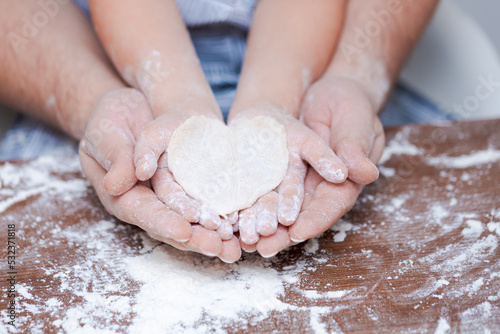 Top view father and child's hand, cut out heart shaped cookies from dough on hands on the background of a wooden table with loose flour. Flat failure.