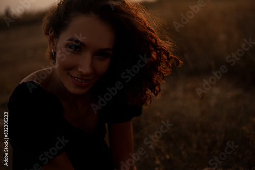 Beautiful sexy woman with natural curly hairs posing in the nature against the field with dry grass and sky