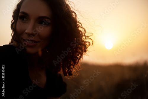 Beautiful sexy woman with natural curly hairs posing in the nature against the field with dry grass and sky