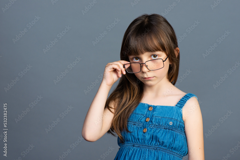 The girl in glasses strictly looks into the camera. Ophthalmologist and children's vision treatment