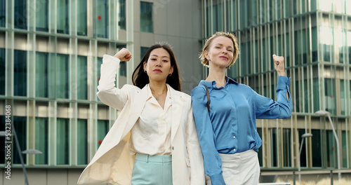 Two business women young empowered women multiethnic looking at camera showing biceps. Feminism , women executives 