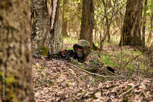 Ukrainian soldier man dressed military disguise camouflage uniform with weapon in woodland at nature background, lying on ground. Male border guard in country border with autogun on war. Copy space