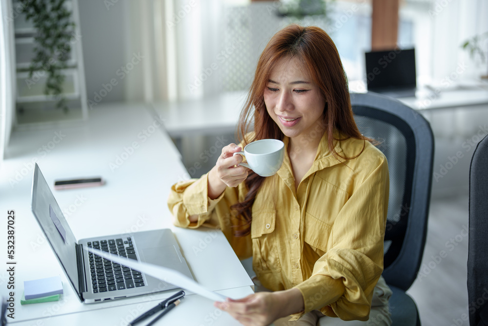 Portrait of a happy Asian woman smiling at her desk during the daytime coffee break