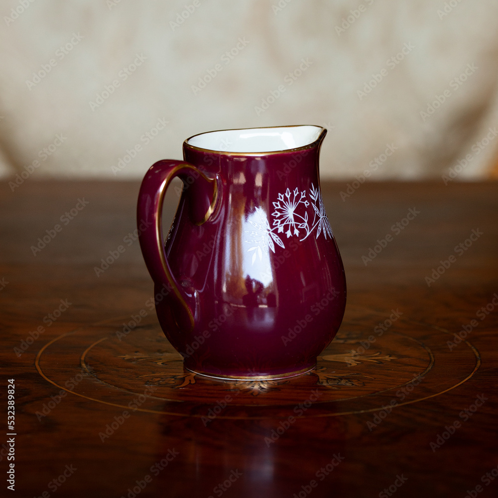 antique dark red porcelain service with national painting. an old Ukrainian-style milk jug in a luxury interior. ceramics close-up antique dark red porcelain service with national painting. an old Ukrainian-style milk jug in a luxury interior. ceramics close-up