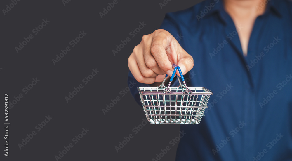 Fototapeta premium A young man is holding a mini shopping cart while standing on a gray background