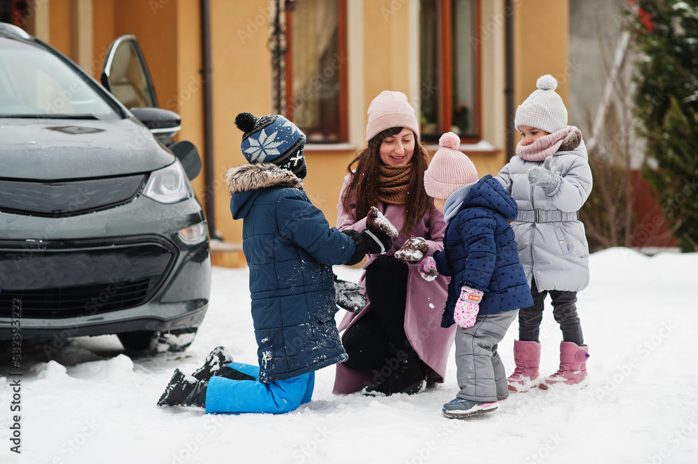Φωτογραφία Young mother play with kids against electric car in the yard of her house at winter