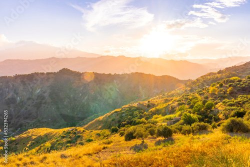 beautiful highland landscape with amazing view from a top with golden grass and green bushes to a canyon with majectic mountains and scenic cloudy sunset on background