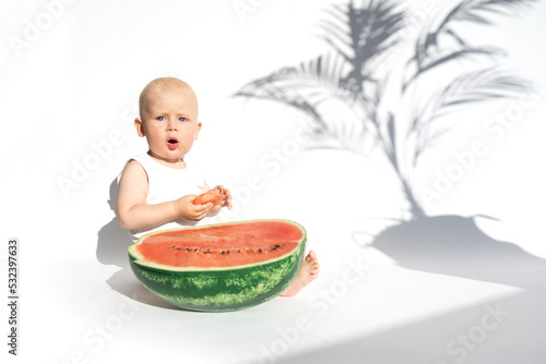 Funny toddler boy playing with ripe watermelon, healthy fruit snack on white background, hot summer day. Organic vegan healthy diet, feeding, solid food concept. Cute baby, child, kid emotins photo