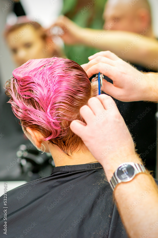 Fototapeta premium Haircut of dyed short pink wet hair of young caucasian woman by a male hairdresser in a barbershop