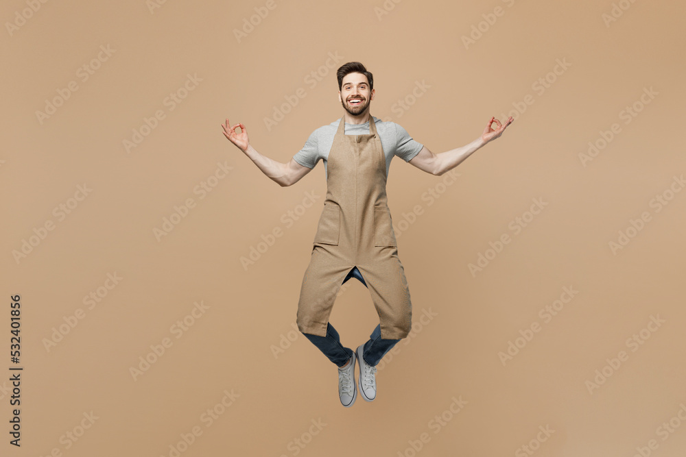 Full body young man barista barman employee wear brown apron work in coffee shop spread hand yoga om gesture meditate calm down isolated on plain light beige background Small business startup concept