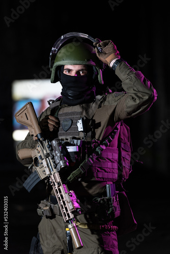 Army soldier in Combat Uniforms with an assault rifle and combat helmet night mission dark background. Blue and purple gel light effect. 