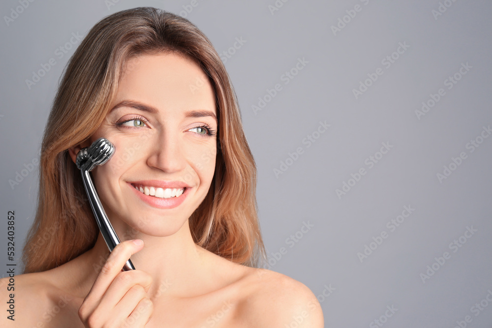 Young woman using metal face roller on light grey background, space for text Young woman using metal face roller on light grey background, space for text