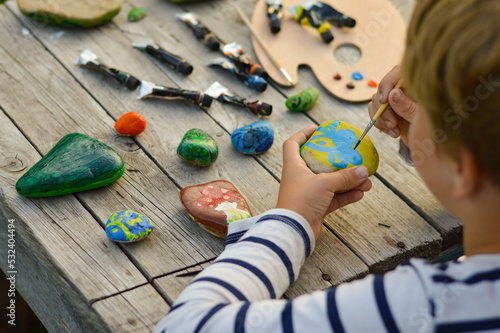 A detailed picture of a child's hands drawing a fungus on a stone with acrylic paints. Home hobbies are authentic. Artwork on stones. photo