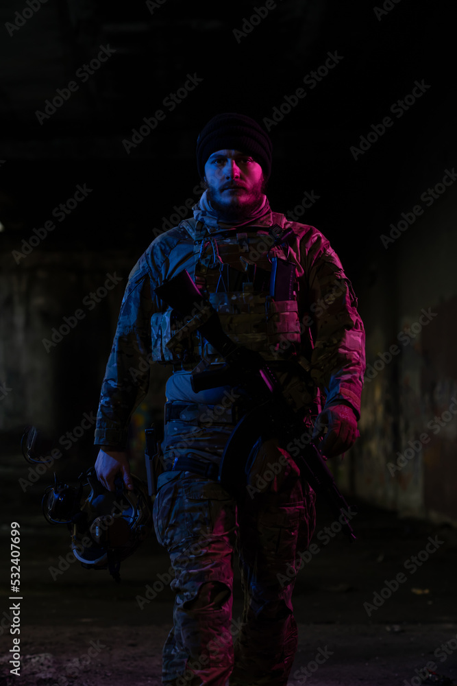 Army soldier in Combat Uniforms with an assault rifle and combat helmet night mission dark background. Blue and purple gel light effect. 