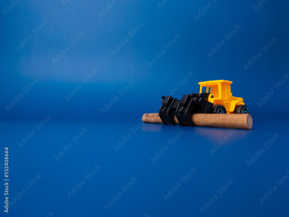 Excavator with wooden stick on blue background with copy space. Conceptual image of illegal logging.
