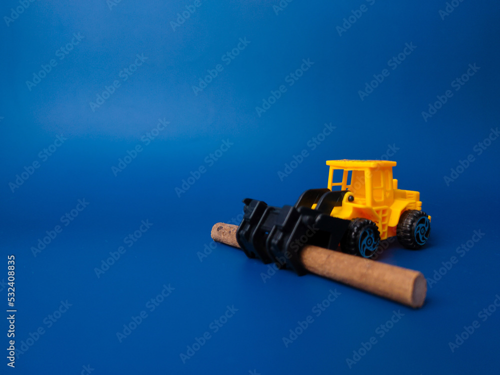 Excavator with wooden stick on blue background with copy space. Conceptual image of illegal logging. Excavator with wooden stick on blue background with copy space. Conceptual image of illegal logging.