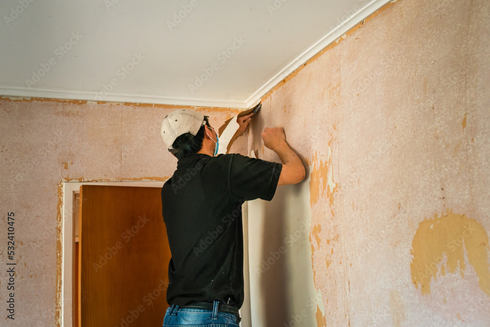 Man removing wallpaper inside an old house