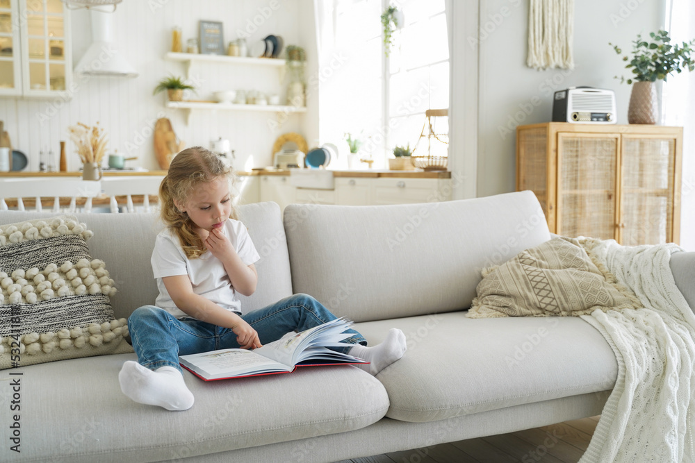 Small kid girl preschooler practices reading fairytale book on sofa at home. Children's education Small kid girl preschooler practices reading fairytale book on sofa at home. Children's education