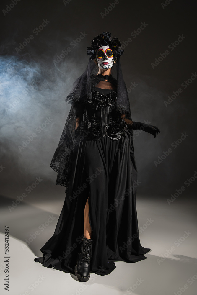 full length of woman in black halloween costume with veil and spooky makeup on dark background with smoke. full length of woman in black halloween costume with veil and spooky makeup on dark background with smoke.