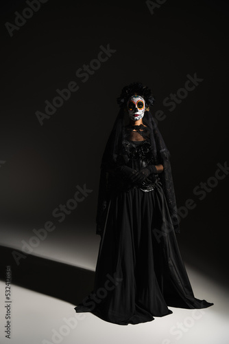 full length of woman in mexican day of dead costume and spooky makeup on black background.