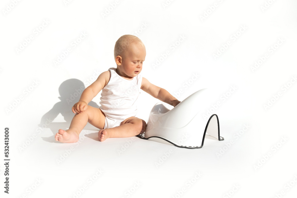 Cute baby in diaper sitting near potty on white background. Toilet and potty training. Hygiene concept. Child toddler gets to use toilet stool. Copy space Cute baby in diaper sitting near potty on white background. Toilet and potty training. Hygiene concept. Child toddler gets to use toilet stool. Copy space