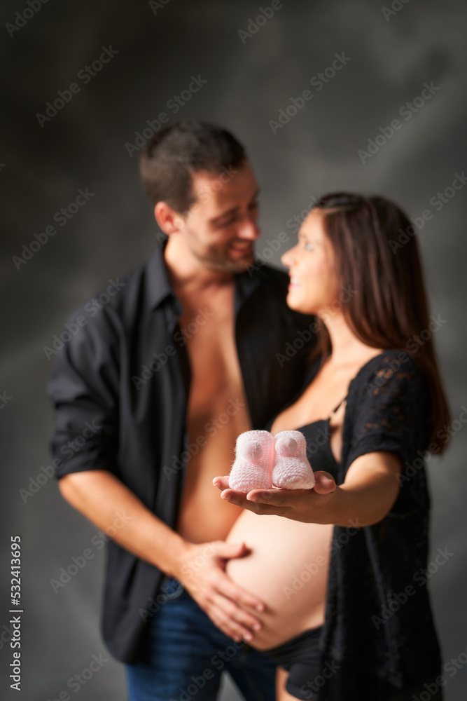 pink baby shoes held by pregnant mother's hand while looking into father's eyes pink baby shoes held by pregnant mother's hand while looking into father's eyes