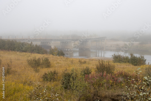 Old destroyed road bridge across the river. Abandoned bridge in the fog. Problems of maintenance and reconstruction of transport infrastructure in remote rural areas. Autumn landscape. Foggy weather.