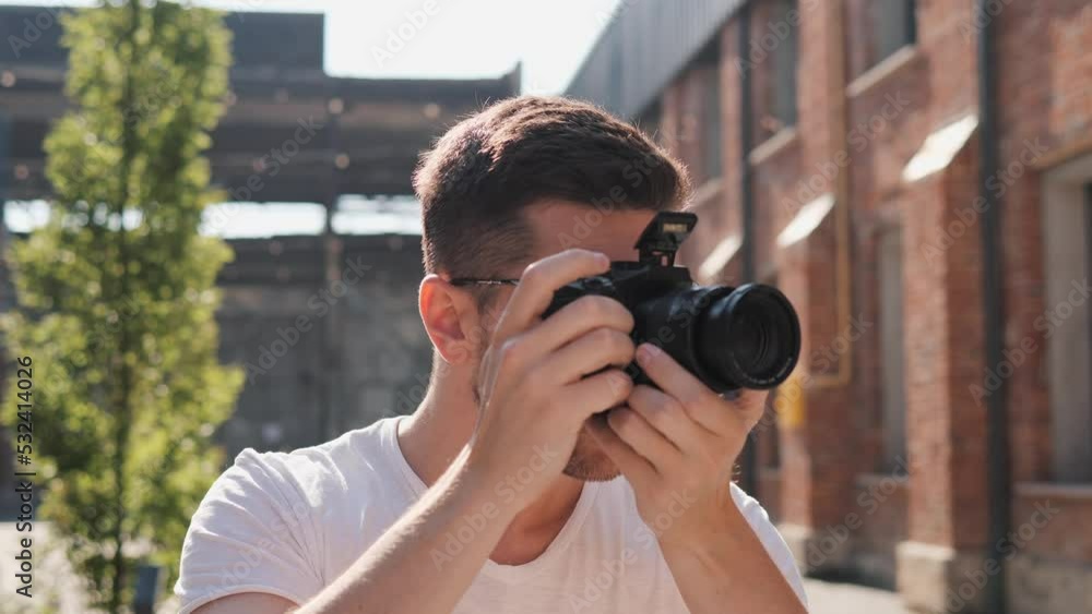 Happy handsome tourist guy with photo camera standing in urban street photographing buildings architecture. Male photographer taking photos on professional camera. Young man enjoys summer time. Happy handsome tourist guy with photo camera standing in urban street photographing buildings architecture. Male photographer taking photos on professional camera. Young man enjoys summer time.