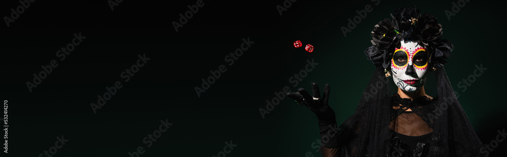Woman in mexican day of dead costume and makeup throwing dice on dark green background, banner. Woman in mexican day of dead costume and makeup throwing dice on dark green background, banner.