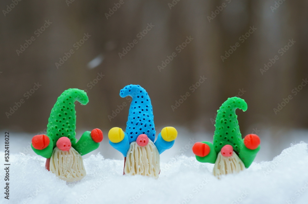Fabulous figures of little dwarfs made of plasticine in the forest against the background of snow. New Year decorations.