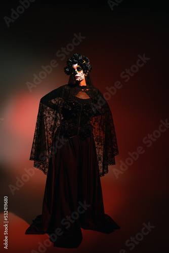 Woman in black costume and creepy halloween makeup standing on burgundy background.
