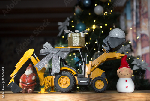 concept of christmas business greetings, new year winter holidays in construction company. toy bulldozer - excavator, gift box, figurine of Santa Claus, snowman against of a decorated Christmas tree