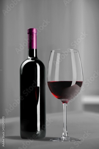 Bottle of tasty red wine with a glass on desk