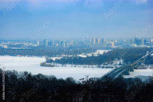 Panoramic view of the Kiev s left bank during a foggy winter day. The Dnieper river is frozen. Trees  road  bridge and buildings  appear in the distance