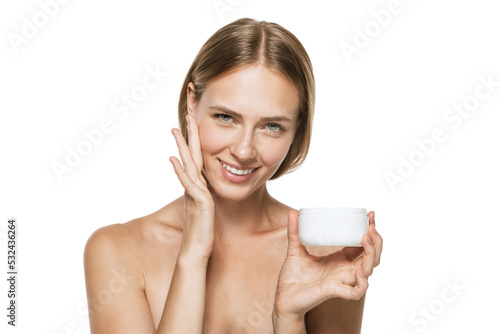 Beauty portrait of happy smiling beautiful half naked girl applying face cream and looking at camera isolated over white background