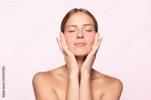 Half-legnth portrait of smiling beautiful girl with naked shoulders applying eye patches isolated over white background