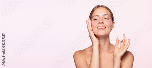 Beauty portrait of happy smiling beautiful half naked girl applying face cream and looking away isolated over white background