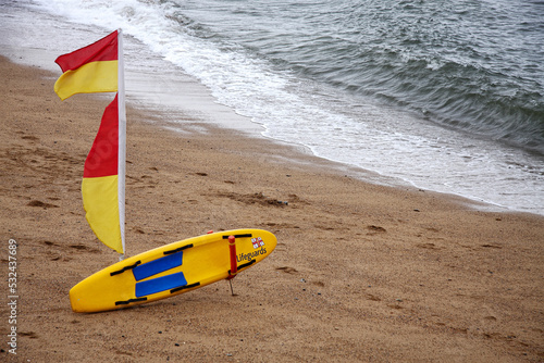 lifeguard raft and yellow and red flag on sandy beach at british seaside
