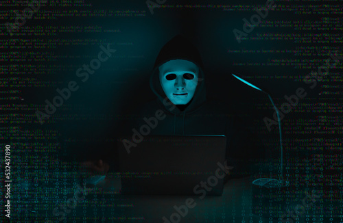 A hacker in black uses a laptop on a desk to hack a system with binary code.Cyber attack, system breaking and malware concept.