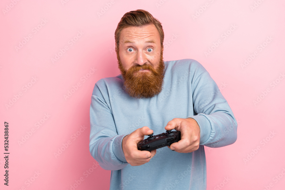 Photo of positive handsome guy with red beard dressed blue pullover holding joystick try difficult level isolated on pink color background Photo of positive handsome guy with red beard dressed blue pullover holding joystick try difficult level isolated on pink color background