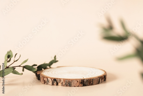 Natural round wooden stand for presentation and exhibitions on pastel beige background. Mock up 3d empty podium with green leaves for organic cosmetic product. Copy space. photo