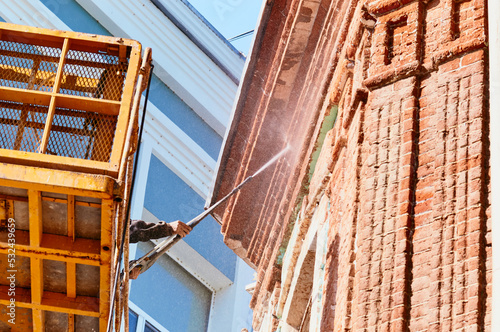 Water jet cleaning of facades. High pressure washing of the facade of a historic building using a hydraulic lift. A worker directs a jet of water at a red brick surface. Splash cloud. Bottom view.