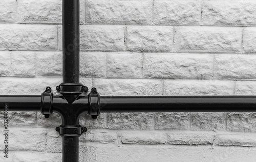 Big black vintage iron drainpipe against a solid white brick wall background.