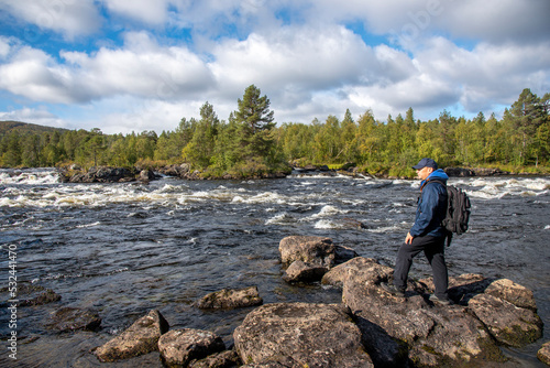 Man hiking in forest near river and looking trough binoculars