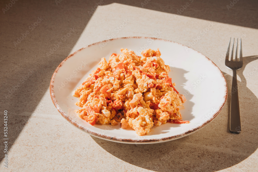 Breakfast, scrambled eggs with tomatoes in a beige plate on a stone table. Top view