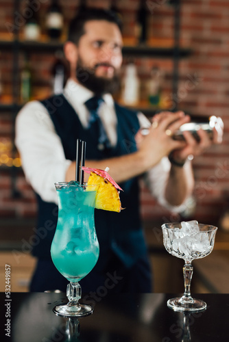blue lagoon cocktail on bar counter, barman shaking cocktail in blurred background