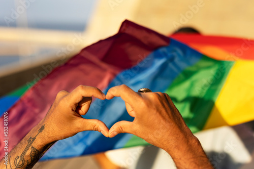 Hands making heart sign in front of rainbow flag.