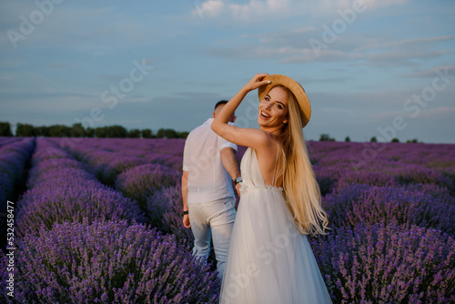 a woman in a white dress and hat and a man in a white shirt are walking in a lavender field..
