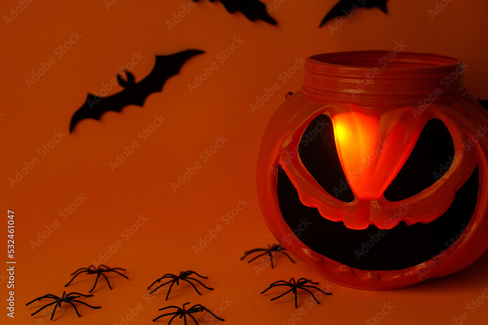Happy Halloween! Scary Jack o lantern candy bucket, black bats and spider decorations on orange background. Spooky Halloween still life. Trick or treat! space for text